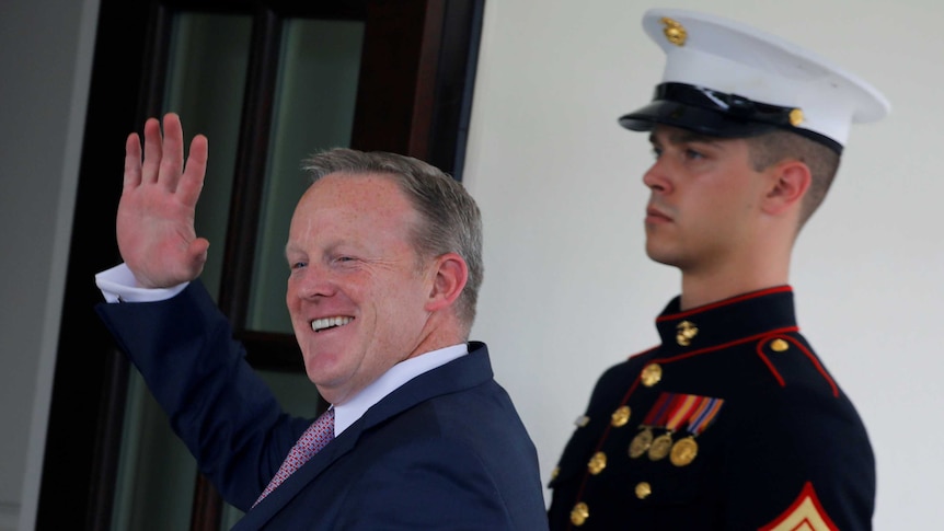 White House Press secretary Sean Spicer waves as he walks into the White House, soldier behind him