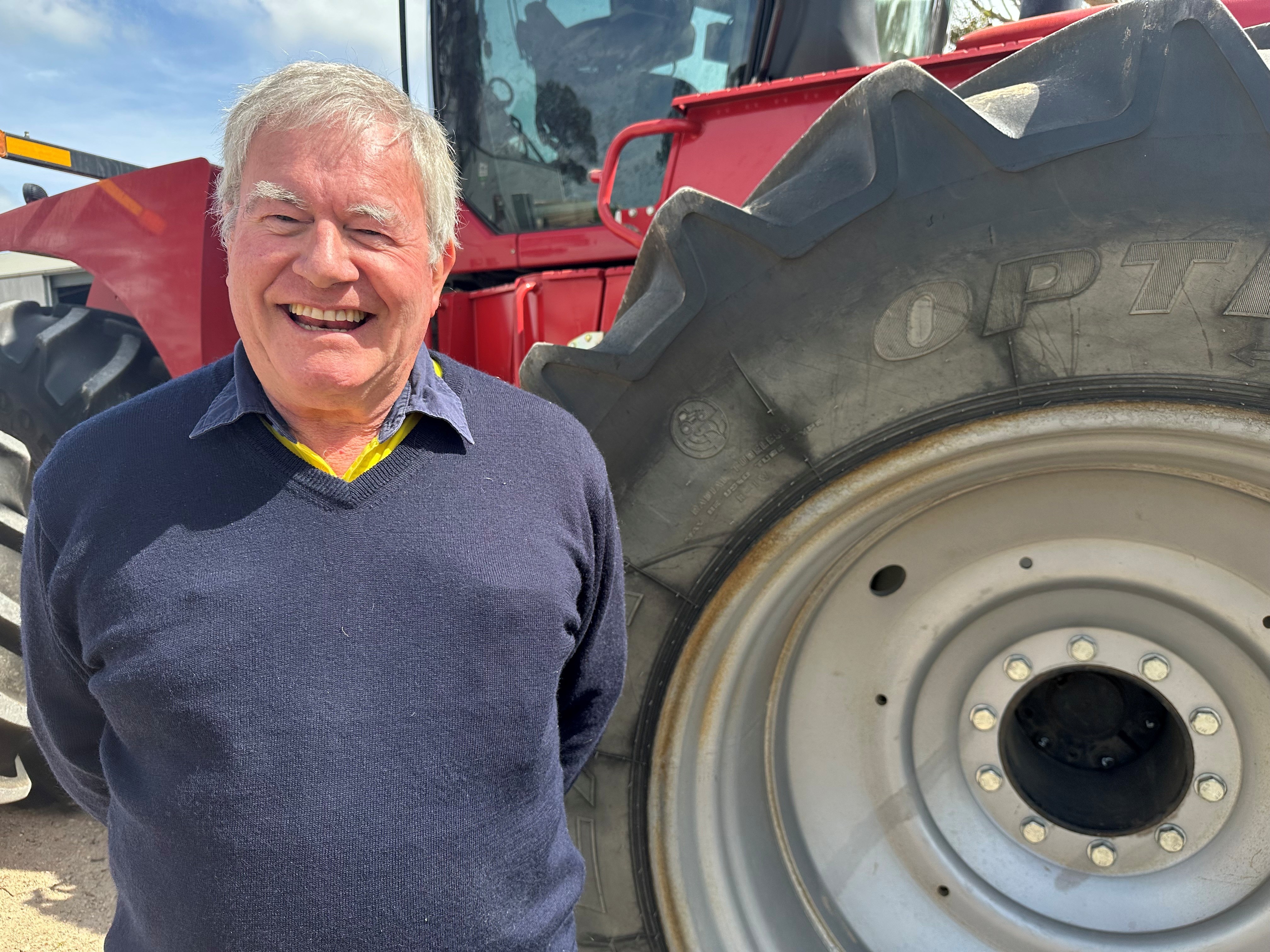 A smiling man in a blue jumper stands in front of a red tractor.