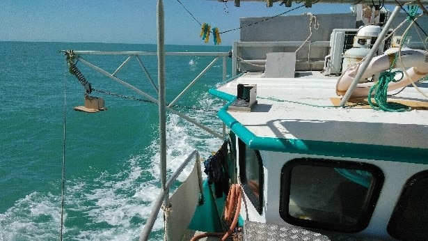 View of the roof, wheelhouse and stabiliser down side of a fishing boat steaming through the water.