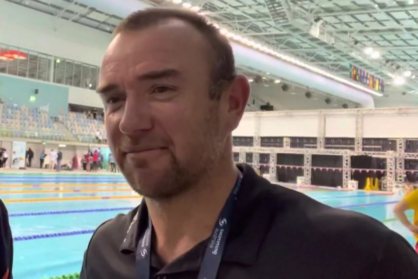 A man wearing a black shirt and standing next to a swimming pool.