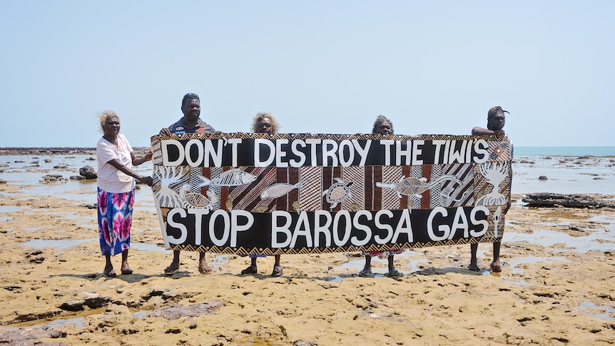 Five Indigenous people hold a sign that reads "Don't destroy the Tiwis, stop Barossa gas" decorated with art.