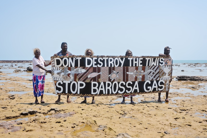 Five Indigenous people hold a sign that reads "Don't destroy the Tiwis, stop Barossa gas" decorated with art.