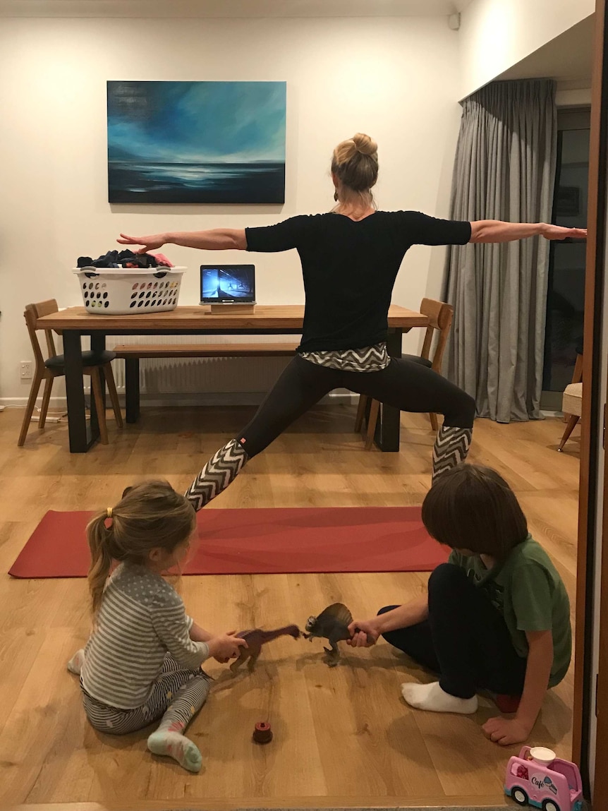 Holly Thorpe does a yoga pose while her kids play on the floor.