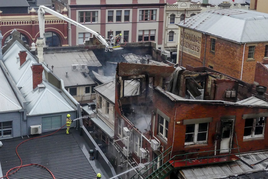 A roof of a city building is badly damaged by fire. You can see the interior of the top floor through tangled metal