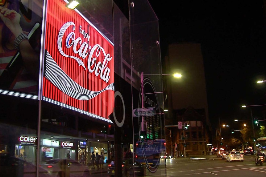 A neon-lit "Enjoy Coca Cola" sign on a street at night.