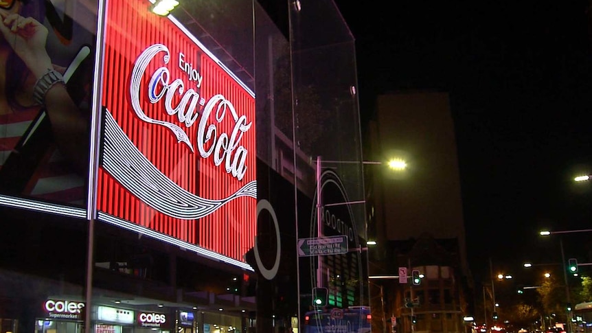 A neon-lit "Enjoy Coca Cola" sign on a street at night.