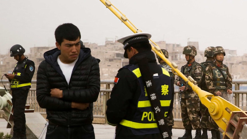 A Chinese police officer speaks to a man as security forces keep watch behind them.