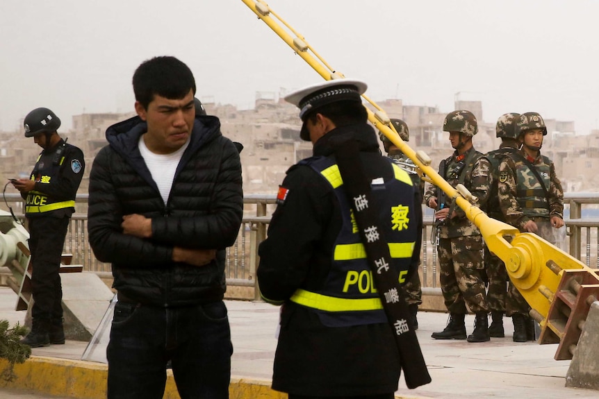 A Chinese police officer speaks to a man as security forces keep watch behind them.