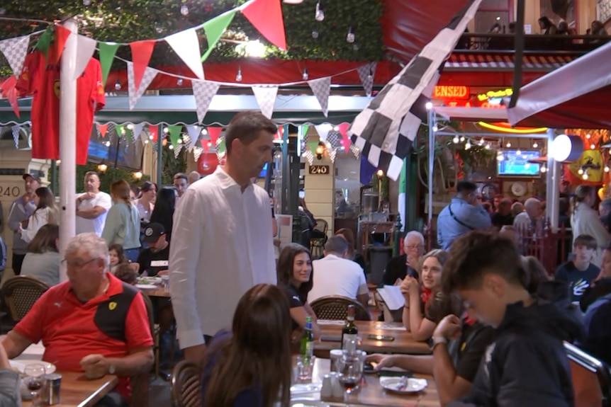 A man stands in the middle of diners under Italian bunting and a chequered flag.
