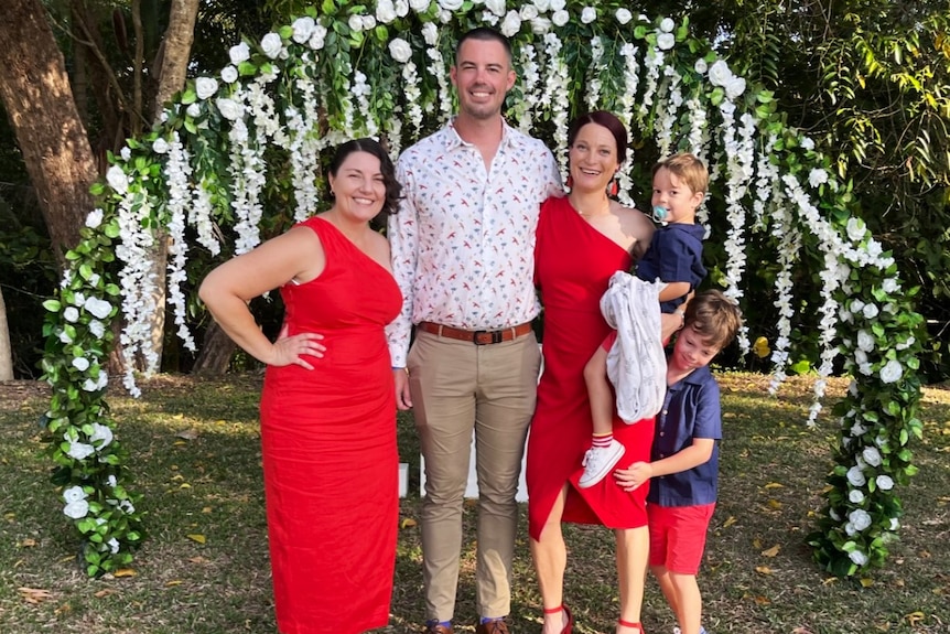 Celebrant stands with newlyweds and two little boys standing under a round flower arbor.