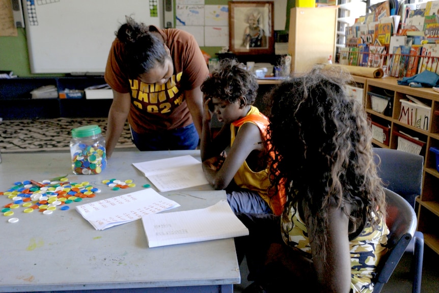 A teacher helps two students in a classroom. 