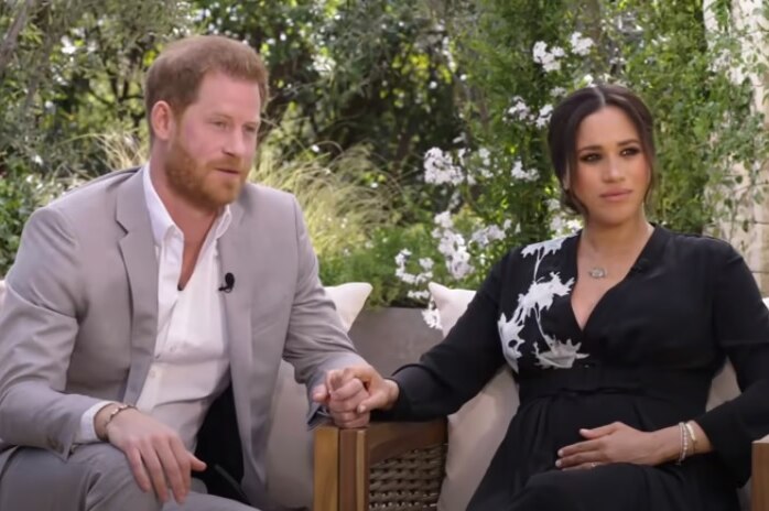 Prince Harry and Meghan Markle sitting on chairs and holding hands.