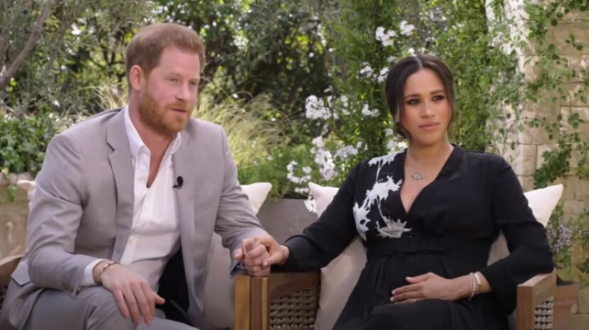 Prince Harry and Meghan Markle sitting on chairs and holding hands.