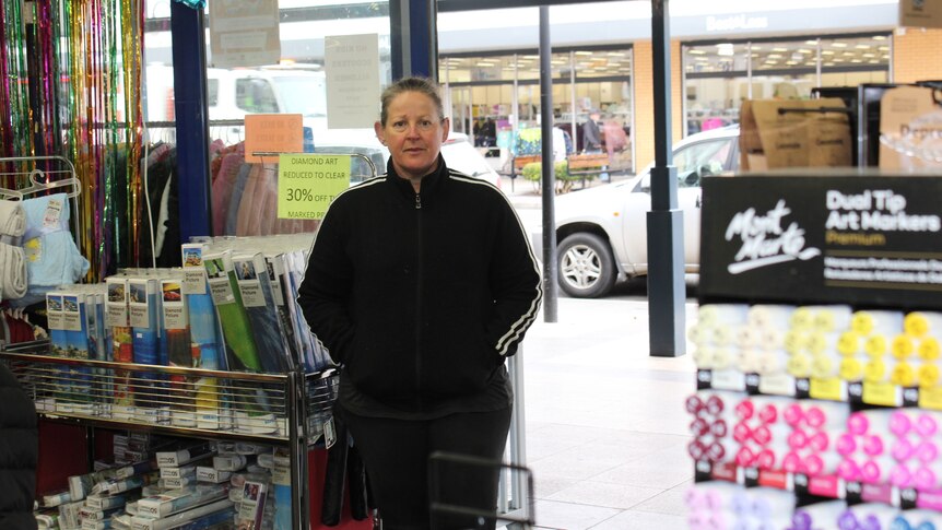 A woman wearing a black tracksuit stands at the entrance to a retail store.