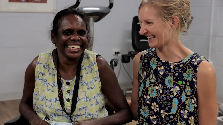 Paulette Bumarda (left) and her support worker Genevieve Agostinelli smile while sitting next to each other.