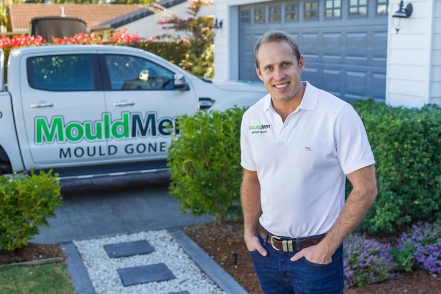 A man in a white shirt stands in front of a car with the words mouldmen in it