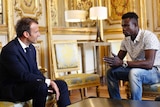 Emmanuel Macron looks at Mamoudou Gassama who is talking to him and gesturing.