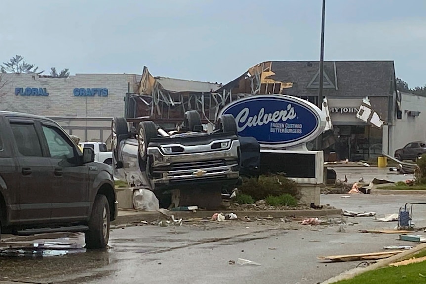 an upturned car an be seen outside a culver's with the shop behind's roof caved in from a storm