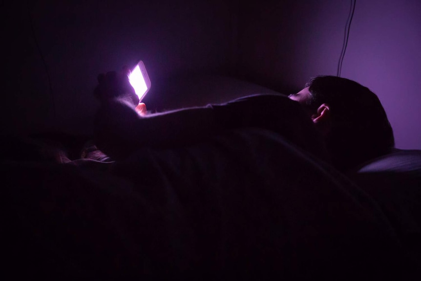 A man lies in bed with using his smartphone.