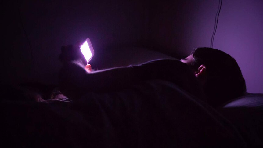 A man lies in bed with using his smartphone.