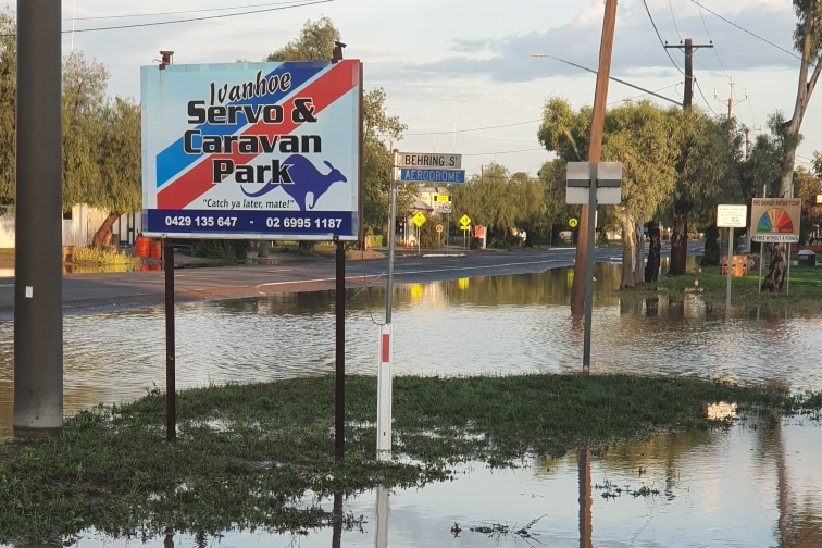 A sign reading 'Ivanhoe servo & caravan park' with large puddles around the sign.
