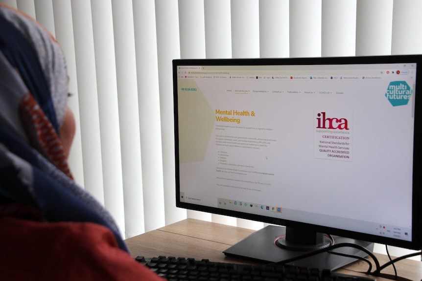 A woman pictured from behind staring at a computer screen.