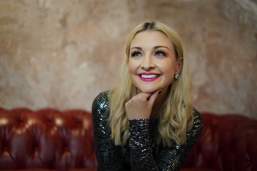 A woman with blonde hair poses for a portrait photo as she wears pink lipstick and a sparkly black top