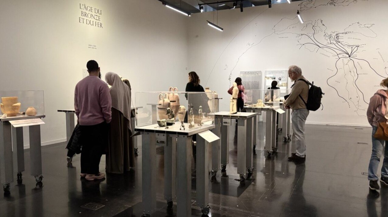 A group of people look at glass displays holding Gazan artefacts in a Paris museum.