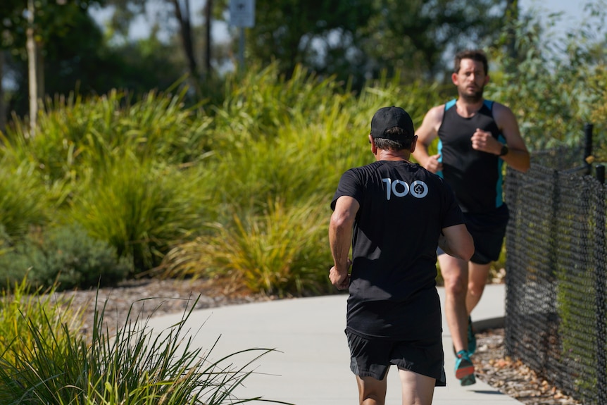 Two men in black T-shirts running in a parkrun.