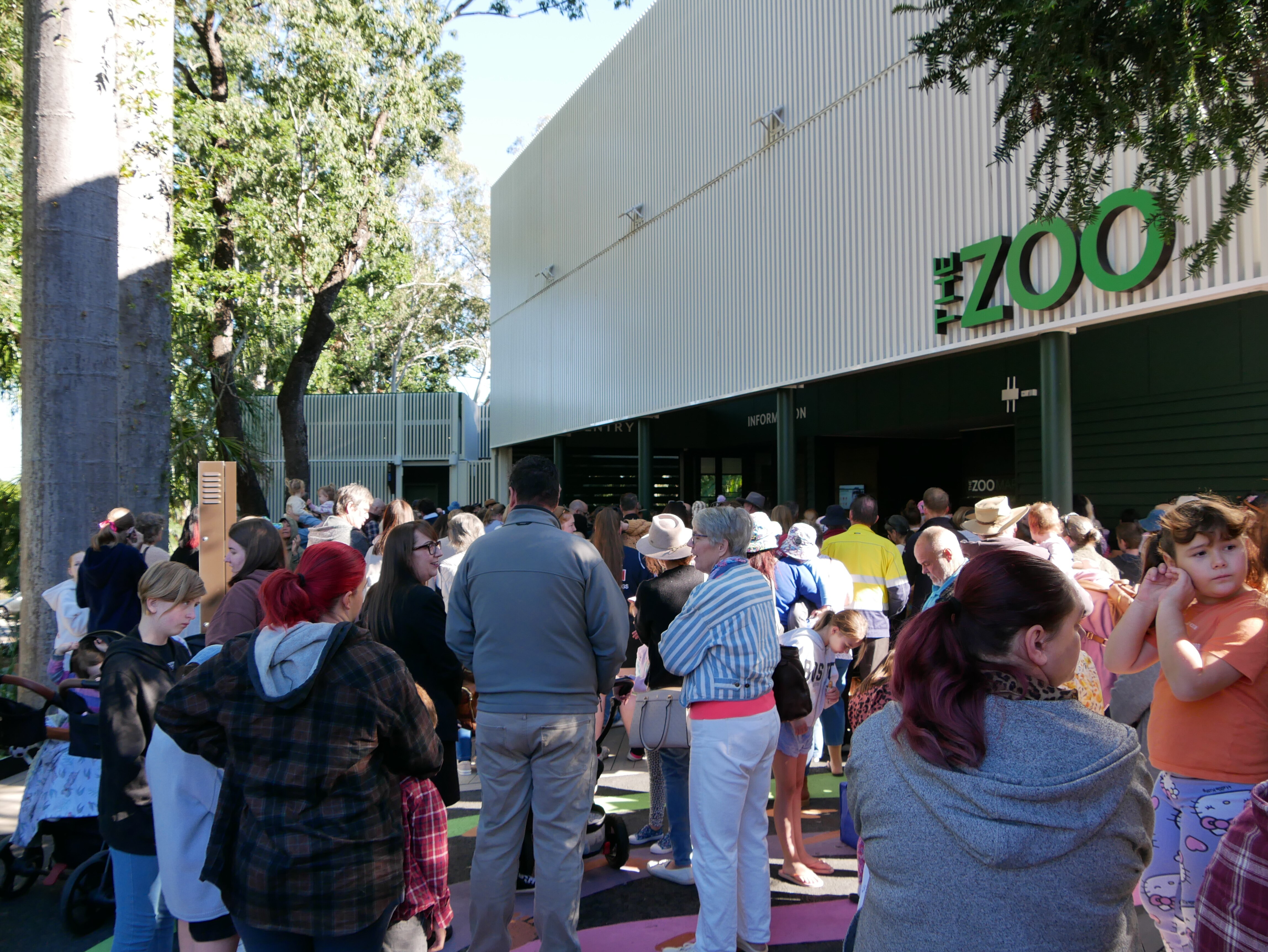 Large crowd of people standing around in jumpers with building in background with sign "the zoo" 