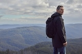 Eric Bana stands looking out over a wild mountain range