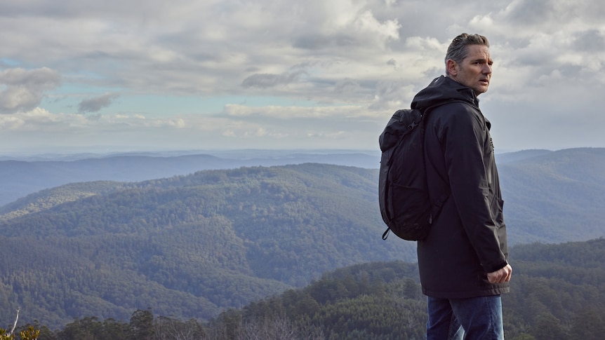 Eric Bana stands looking out over a wild mountain range