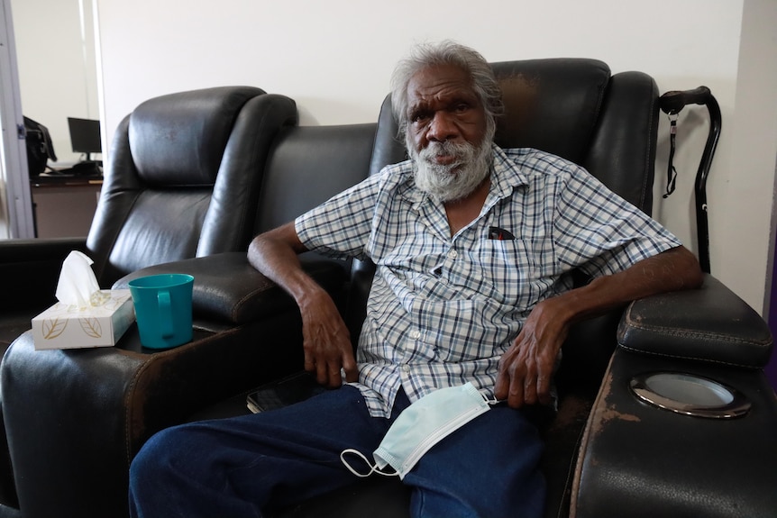 An Aboriginal man sits in a large black armchair. 