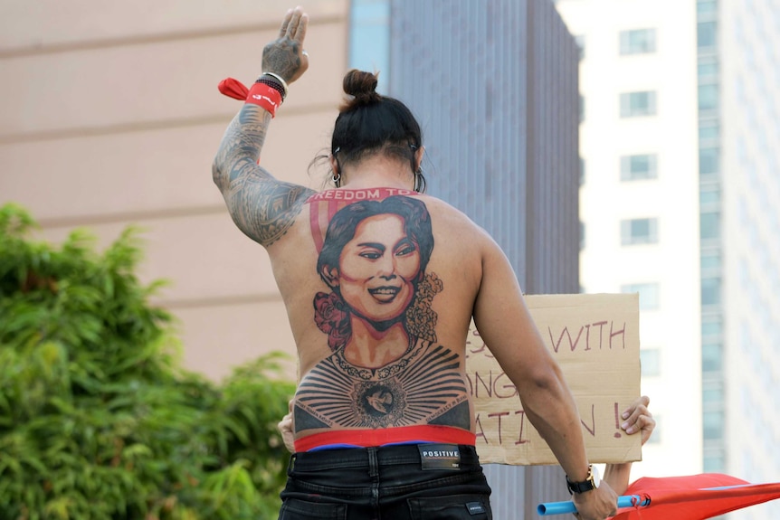 A man with a tattoo of Aung San Suu Kyi holds up a three-finger salute.