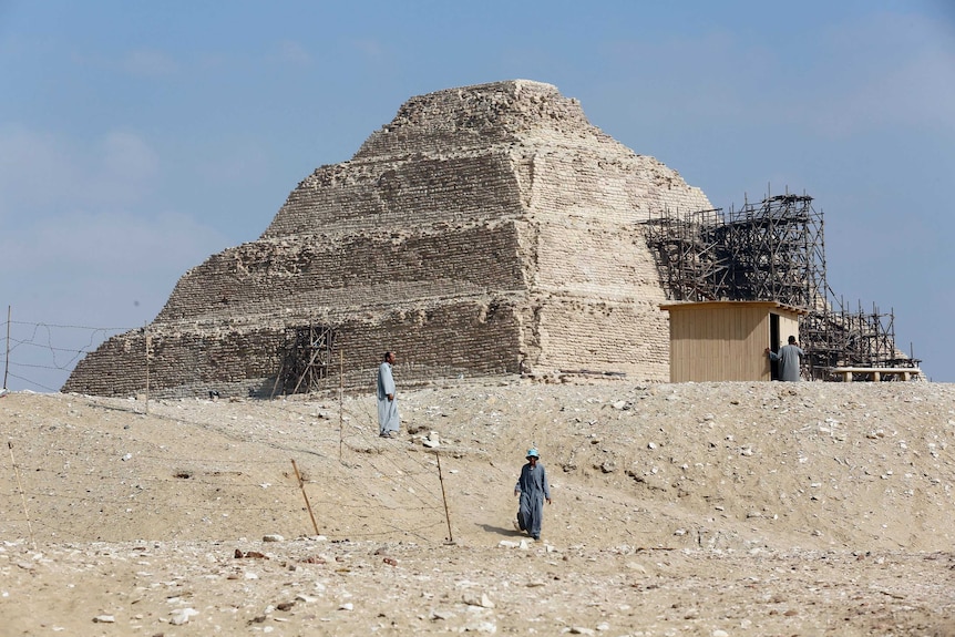 Two men are seen outside a step pyramid.