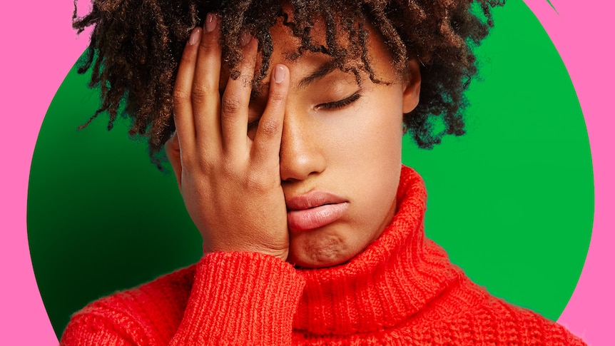 African American woman with red jumper has her palm on her face looking exhausted.