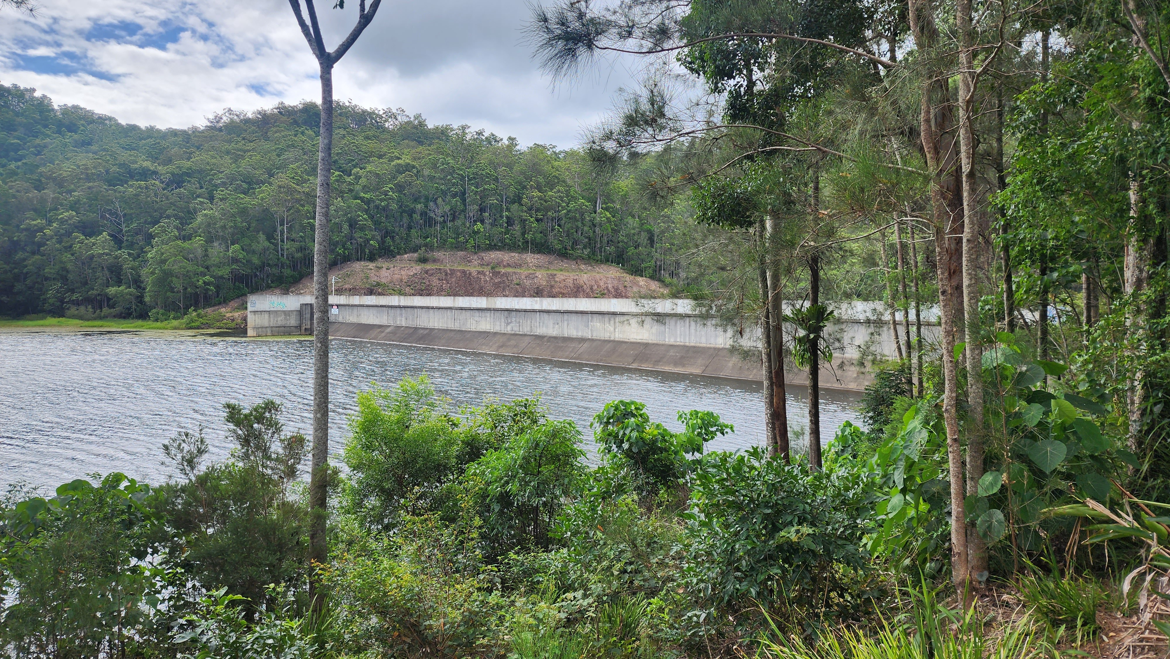 A body of water dammed in by a concrete wall, with hills in the background.
