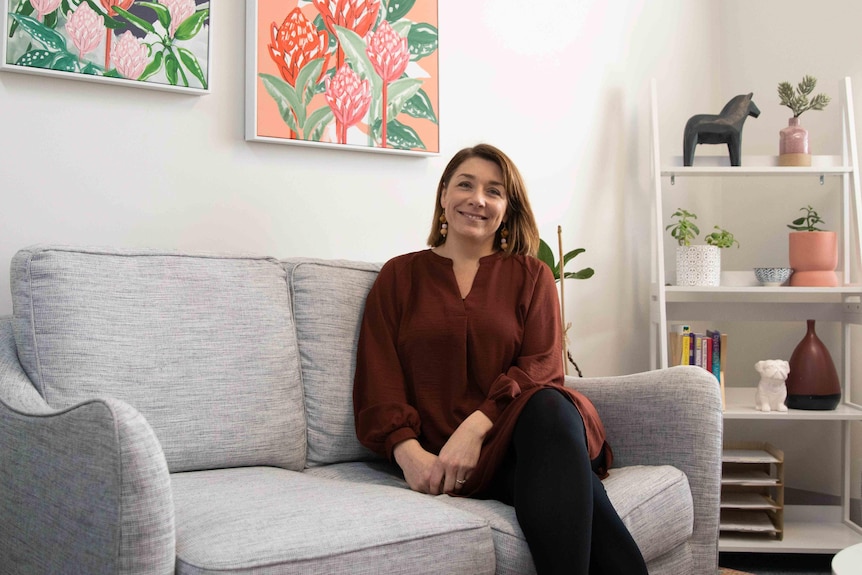 Maddi Derrick, sitting on a grey couch looking at the camera and smiling