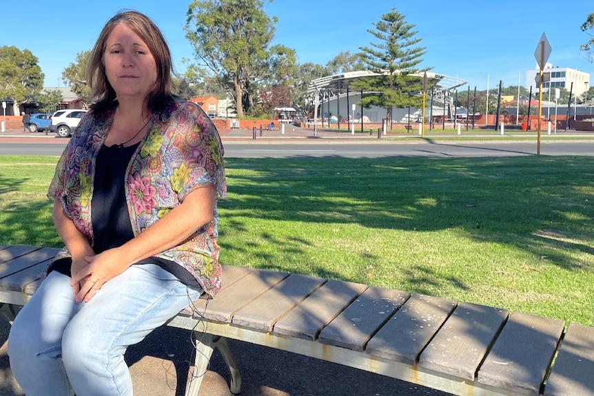 A woman sitting on a bench with cars and a road behind her 