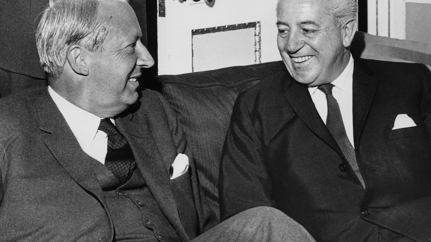 black and white. two silver haired men sitting close together and laughing