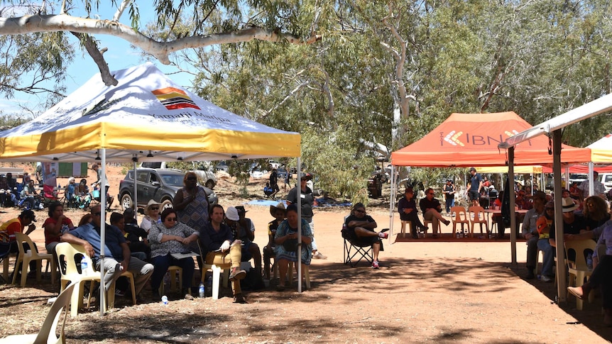 Members of the Yule River community sit under marquees with trees all around.