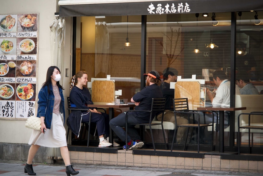 A woman in a face mask walks past a ramen restaurant