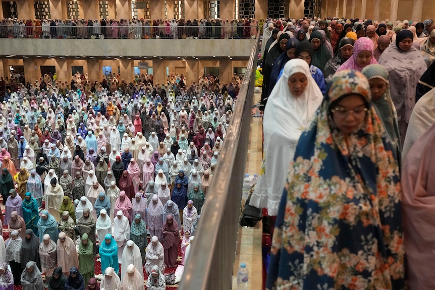 People pray shoulder to shoulder across two levels of a mosque