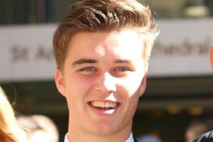 A young man with his blond hair combed back smiles at the camera