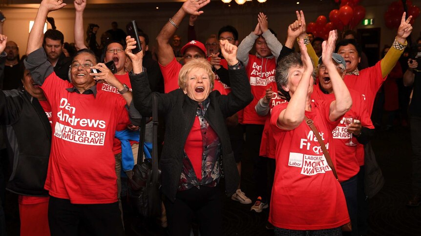 People in red 'Daniel Andrews' shirts cheer at a function centre.