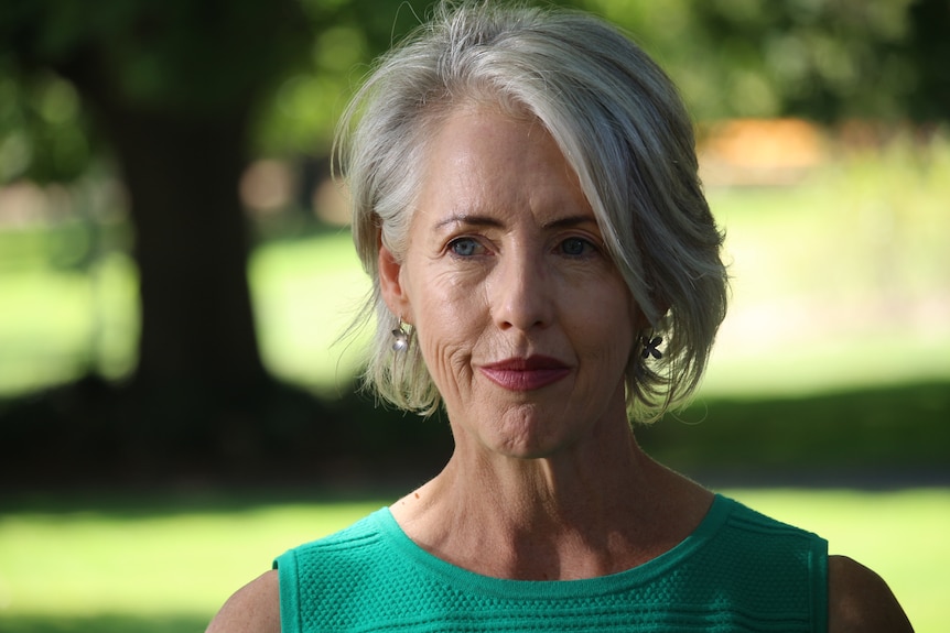 A woman with short white hair and a green top stands outside.