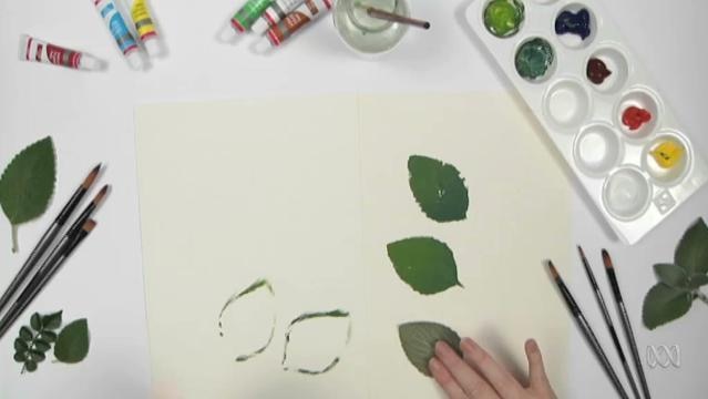 Hand uses leaf as a stamp to make leaf-shape impressions on paper