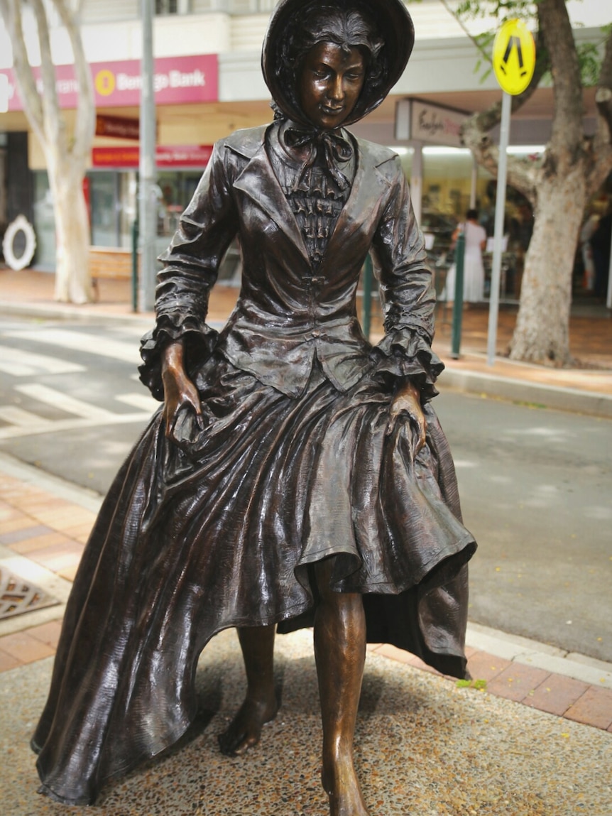 A bronze statue of a woman wearing a long dress and hat