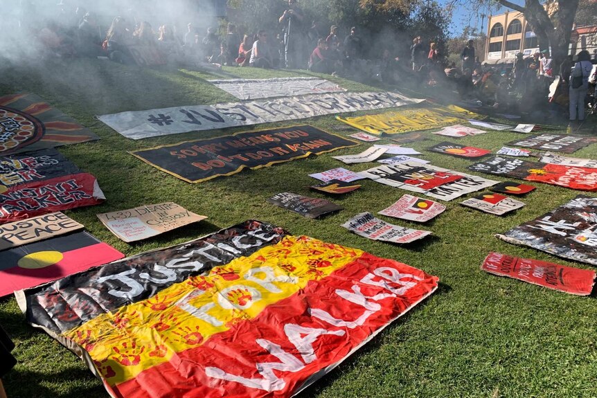 signs lay on grass in front of people sitting as smoke rises