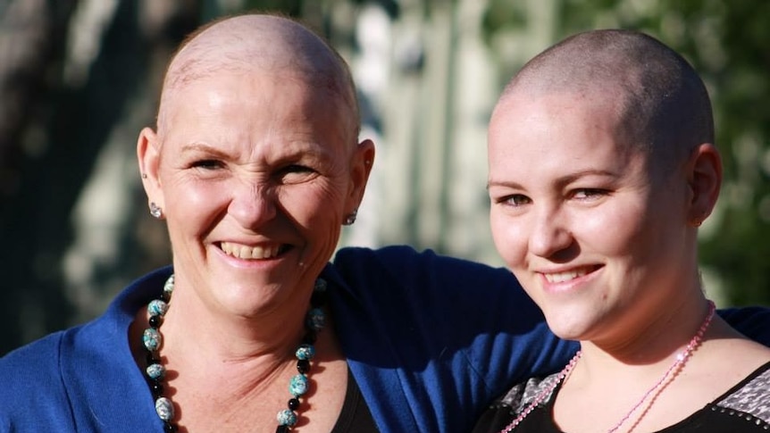 Two women with shaved heads embrace